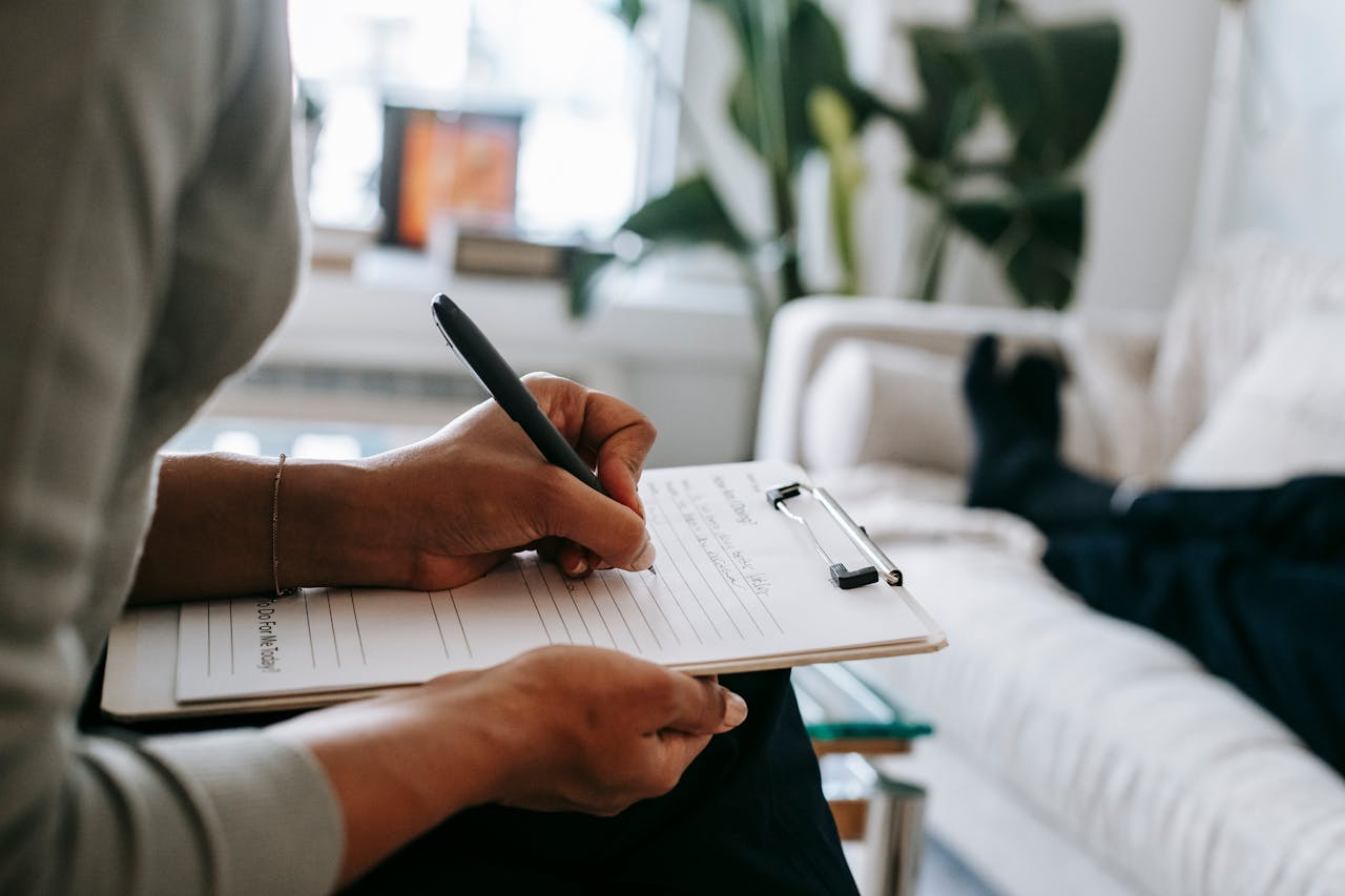 Servizi Unrecognizable ethnic female therapist taking notes on clipboard while filling out form during psychological appointment with anonymous client lying on blurred background